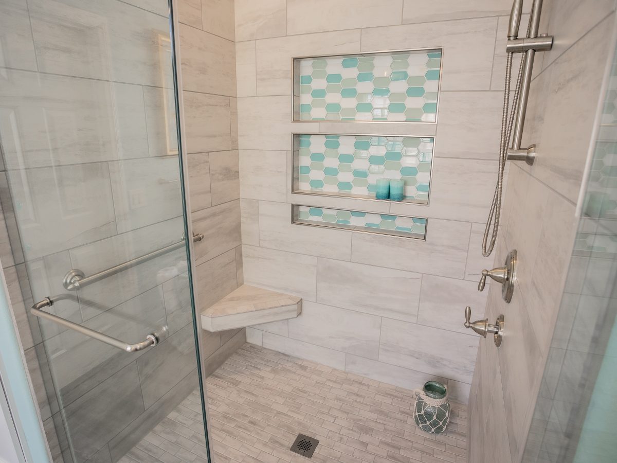 Coastal primary bathroom shower with stone-look porcelain tile, teal hex mosaic niches, and brushed nickel fixtures — Reveal Interior Design Las Vegas