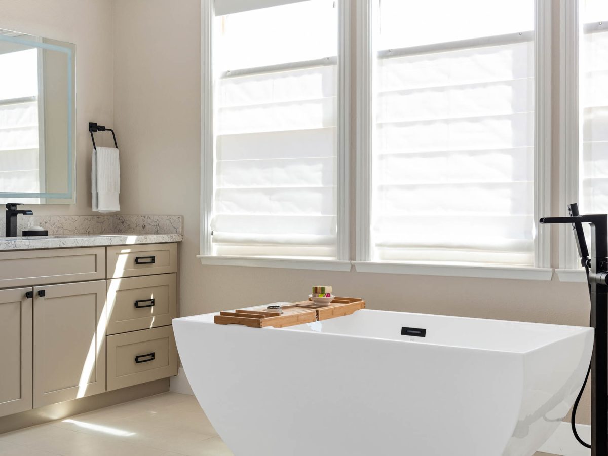 Primary bathroom with freestanding soaking tub, warm beige cabinetry, and quartz countertops — Reveal Interior Design Las Vegas