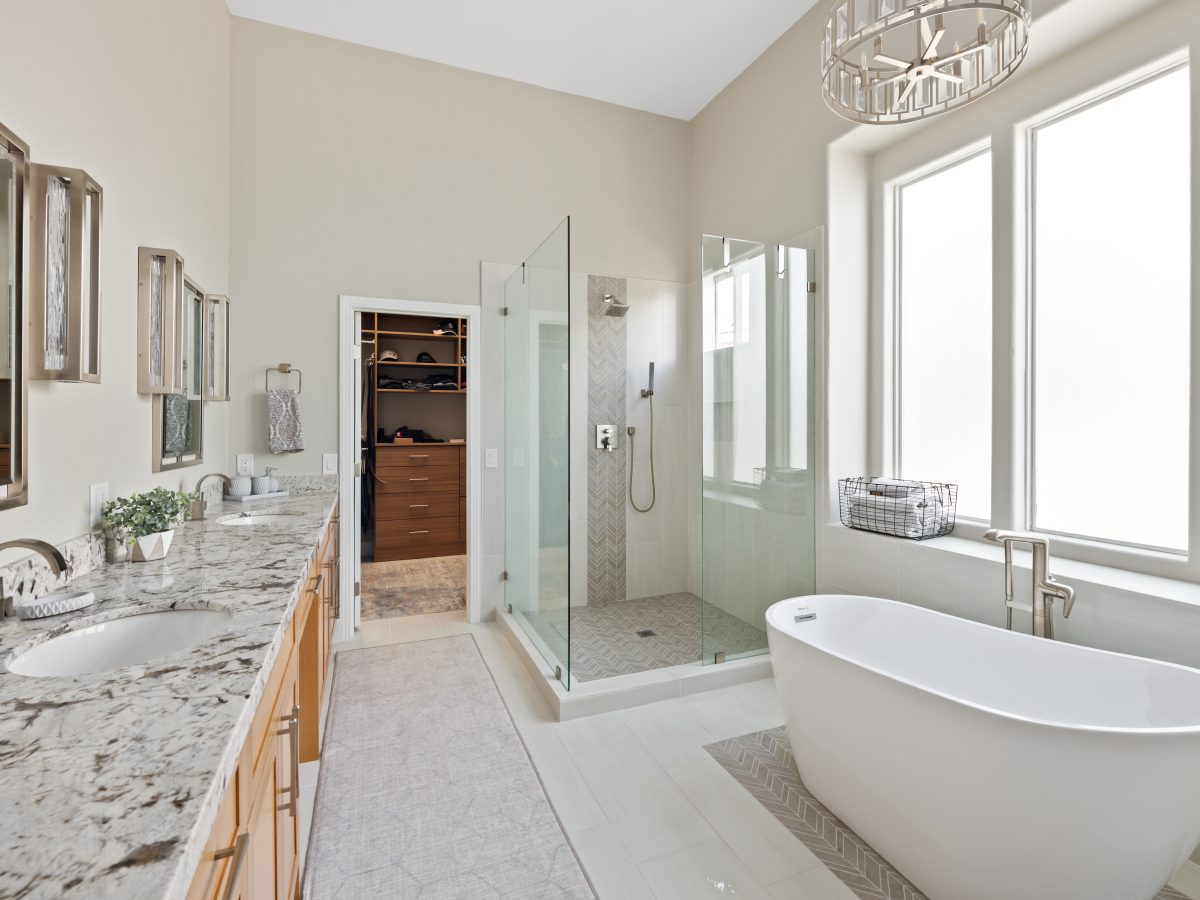 Primary bathroom with granite dual vanity, freestanding soaking tub, and glass walk-in shower — Reveal Interior Design Las Vegas