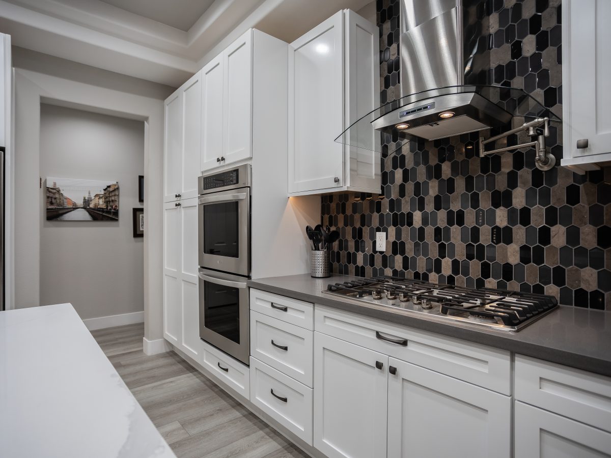 Contemporary kitchen with white shaker cabinets, elongated hex mosaic backsplash, and stainless steel appliances — Reveal Interior Design Las Vegas
