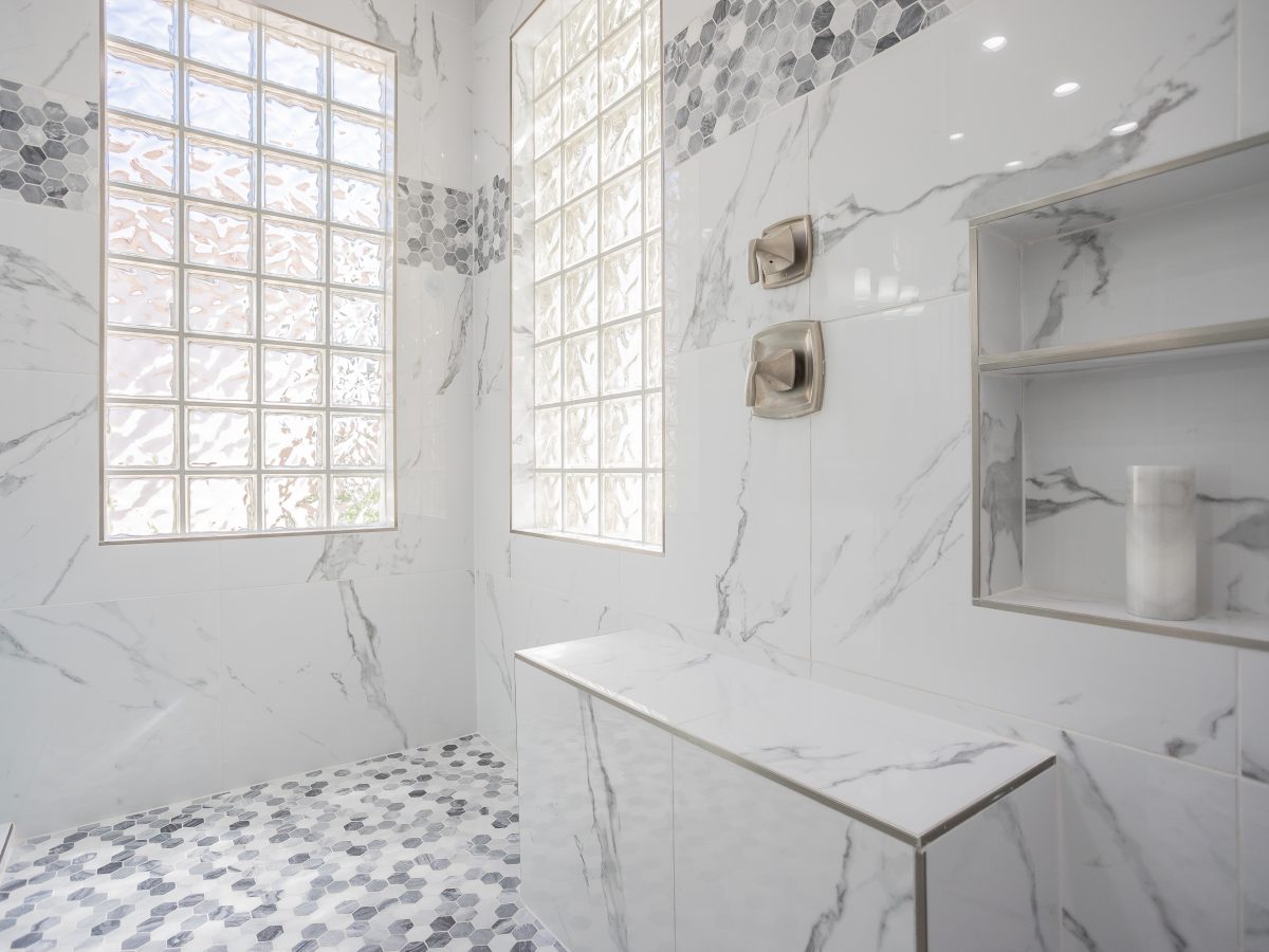 Expansive primary bathroom shower with marble-look porcelain tile walls and geometric mosaic accents — Reveal Interior Design Las Vegas