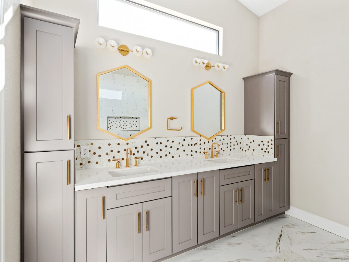 Primary bathroom with taupe shaker cabinetry, gold fixtures, and calacatta-look mosaic tile backsplash — Reveal Interior Design Las Vegas
