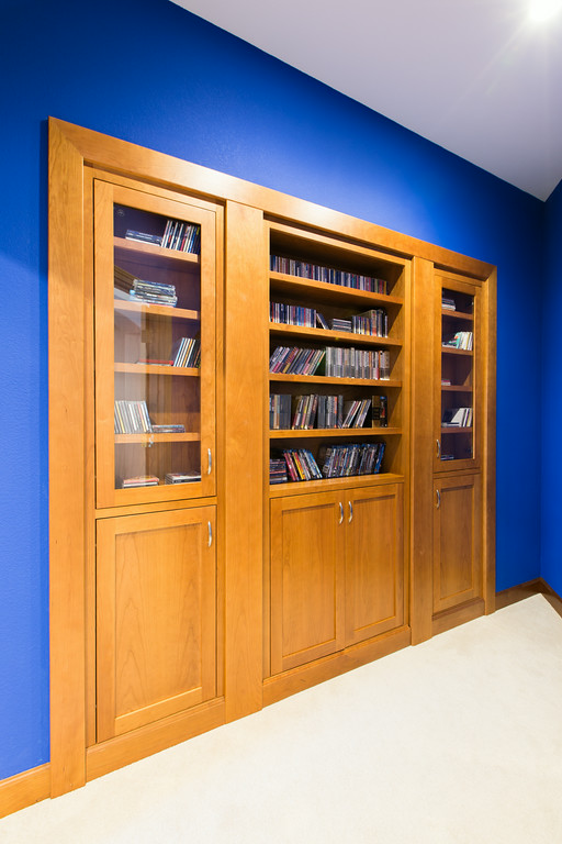 Home theater with deep blue walls, maple millwork accents, and hidden bookcase door — Reveal Interior Design Las Vegas
