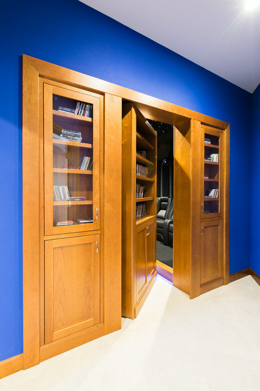 Home theater with hidden maple bookcase door, cobalt blue walls, and raised seating platform — Reveal Interior Design Las Vegas