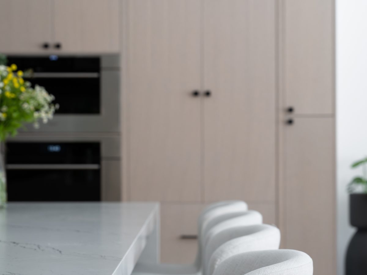 Luxury kitchen with white-washed oak cabinetry, black-veined white quartz island, and upholstered counter stools — Reveal Interior Design Las Vegas