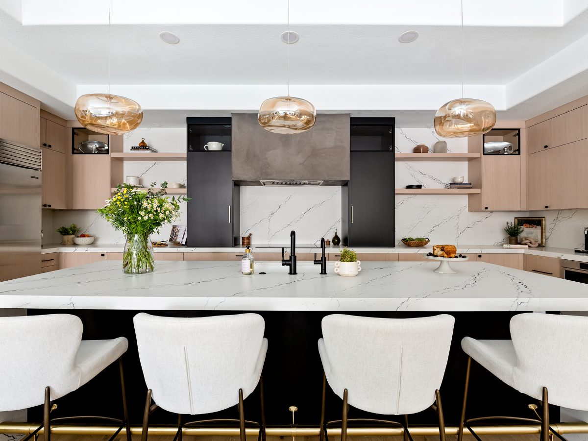 Open-concept kitchen with white-washed oak cabinetry, black quartz island, and amber pendant lighting — Reveal Interior Design Las Vegas