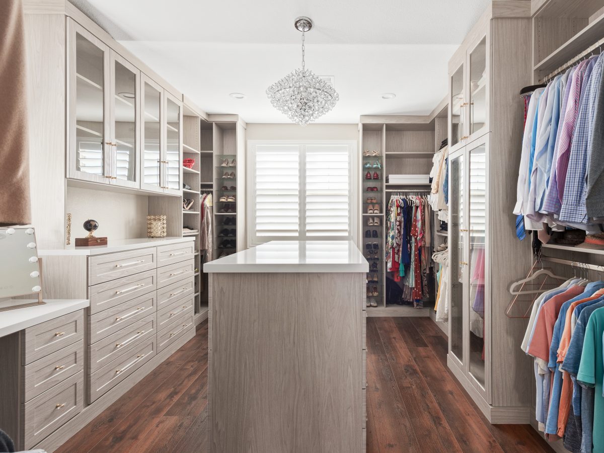 Large walk-in closet with taupe cabinetry, quartz island, and crystal chandelier — Reveal Interior Design Las Vegas