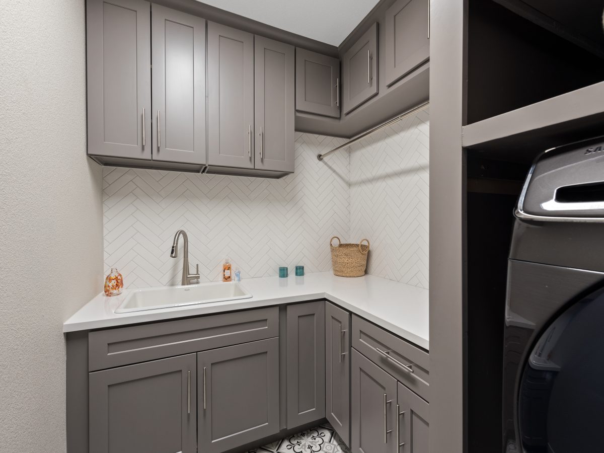 Laundry room with taupe shaker cabinetry, white quartz counters, and herringbone subway tile — Reveal Interior Design Las Vegas
