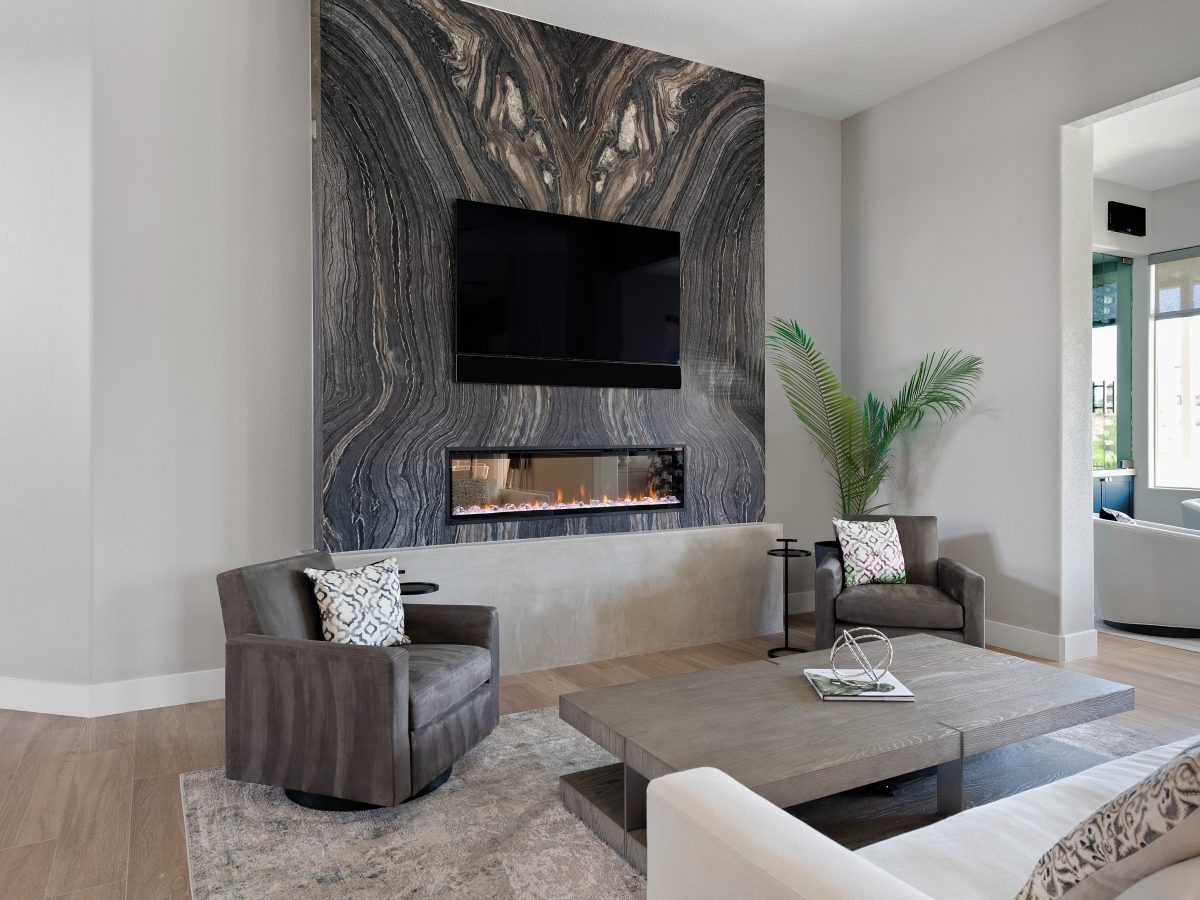 Living room with bookmatched leathered quartzite feature wall, linear fireplace, and modern swivel seating — Reveal Interior Design Las Vegas