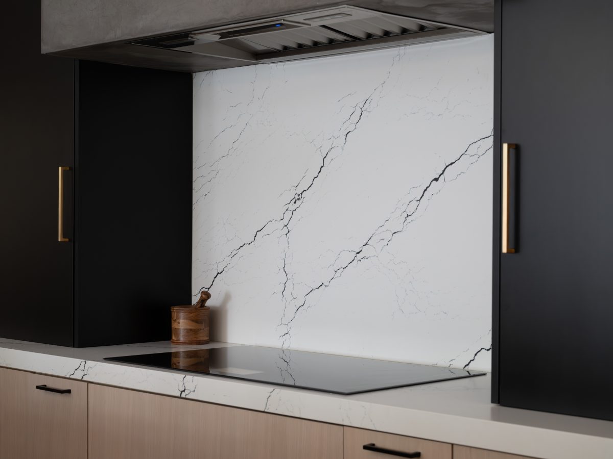 Modern kitchen with black veined white quartz backsplash, matte black upper cabinetry, and gold hardware — Reveal Interior Design Las Vegas