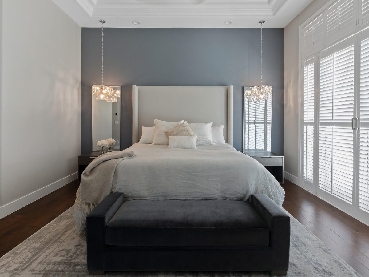 Primary bedroom with slate blue accent wall, tall upholstered headboard, and pendant lighting — Reveal Interior Design Las Vegas