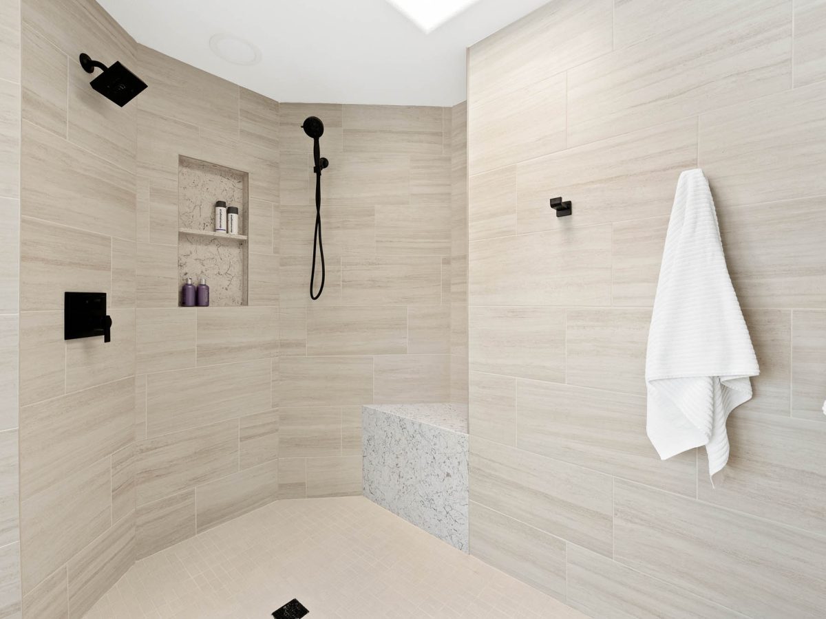 Primary bathroom angled walk-in shower with built-in bench, dual-level niche, and matte black fixtures — Reveal Interior Design Las Vegas