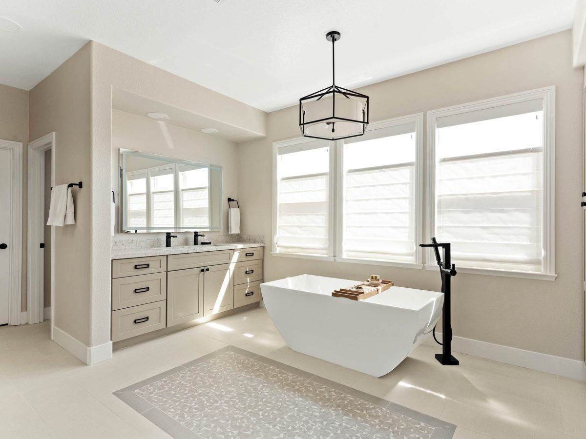 Primary bathroom with freestanding soaking tub, warm beige cabinetry, and quartz countertops — Reveal Interior Design Las Vegas