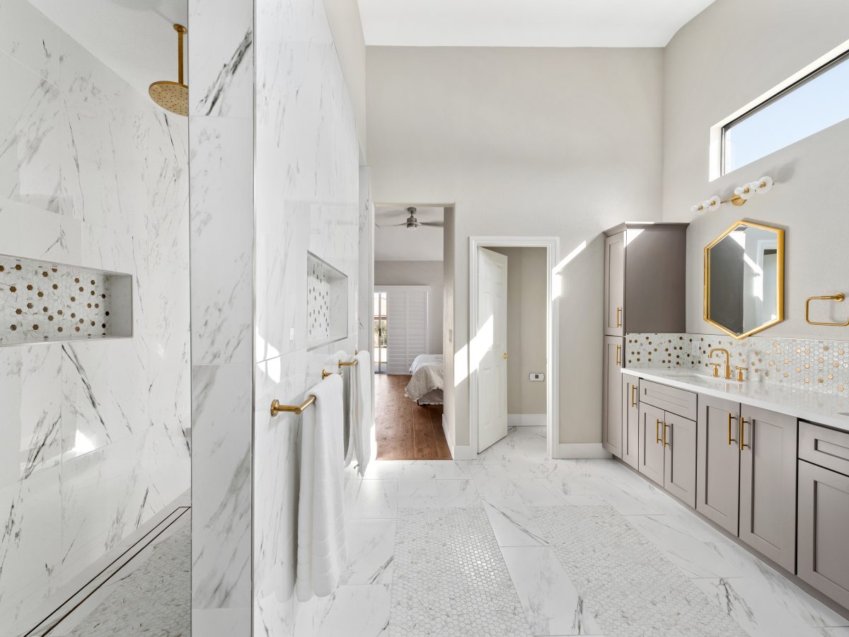 Primary bathroom with calacatta porcelain tile, taupe shaker cabinetry, and gold fixtures — Reveal Interior Design Las Vegas