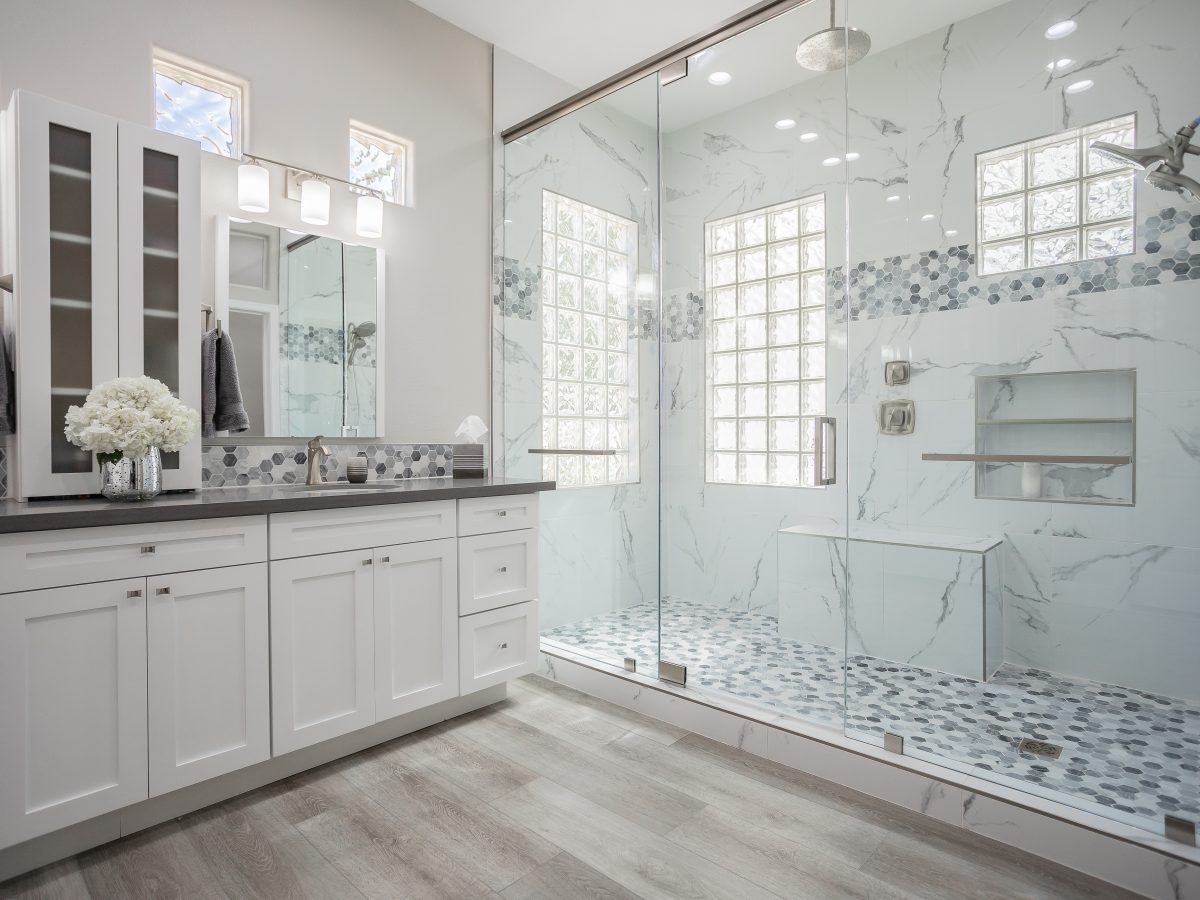 Primary bathroom with marble-look porcelain shower, white shaker vanity, and greige quartz countertops — Reveal Interior Design Las Vegas