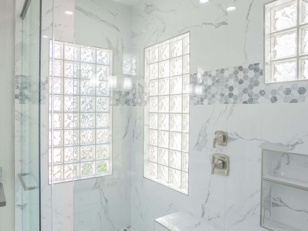 Primary bathroom with marble-look porcelain shower walls, geometric mosaic tile accents, and ceiling-mount rain showerhead — Reveal Interior Design Las Vegas