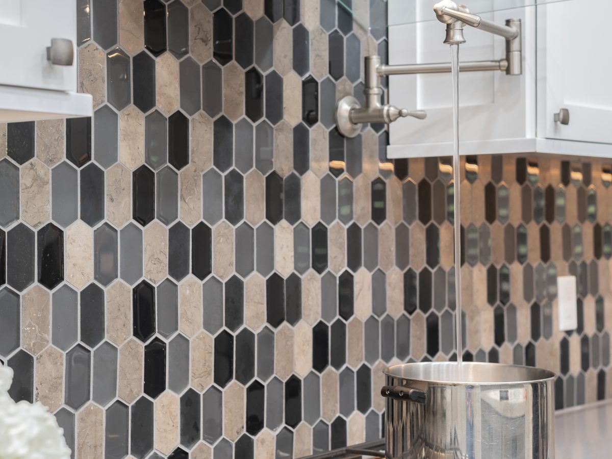 Kitchen cooktop with elongated hex glass and stone mosaic backsplash and pot filler — Reveal Interior Design Las Vegas