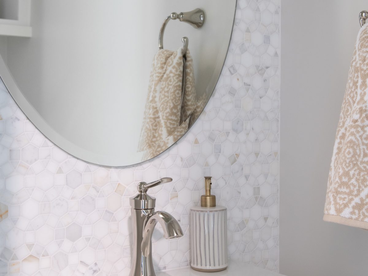 Powder bath with geometric marble mosaic tile wall, oval mirror, and polished nickel faucet — Reveal Interior Design Las Vegas