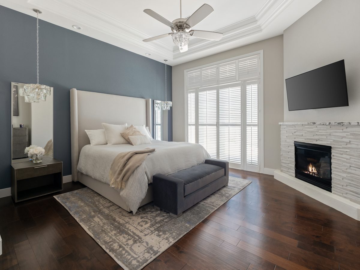 Primary bedroom with slate blue accent wall, cherry engineered wood floors, and stone fireplace — Reveal Interior Design Las Vegas