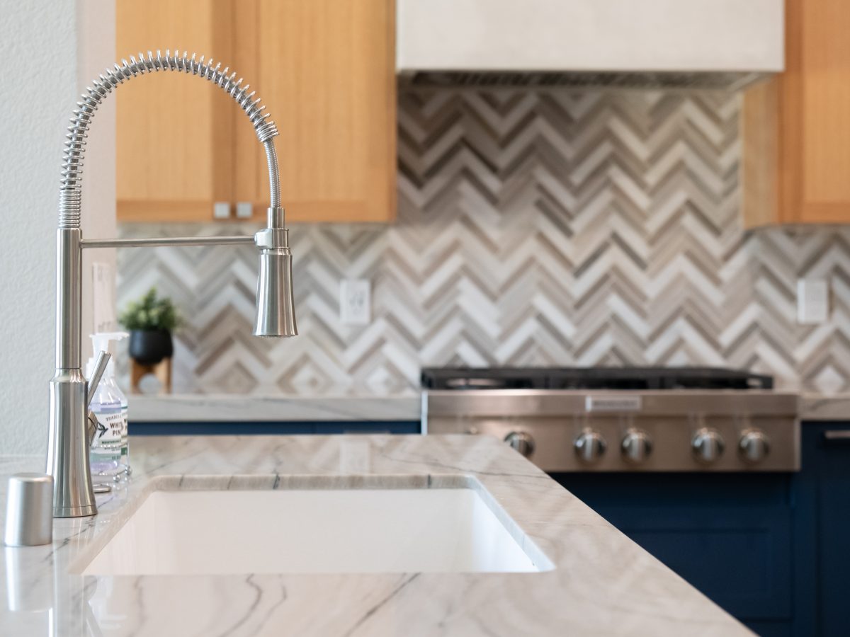 Kitchen with quartzite island countertop, brushed nickel spring faucet, and stone herringbone mosaic backsplash — Reveal Interior Design Las Vegas