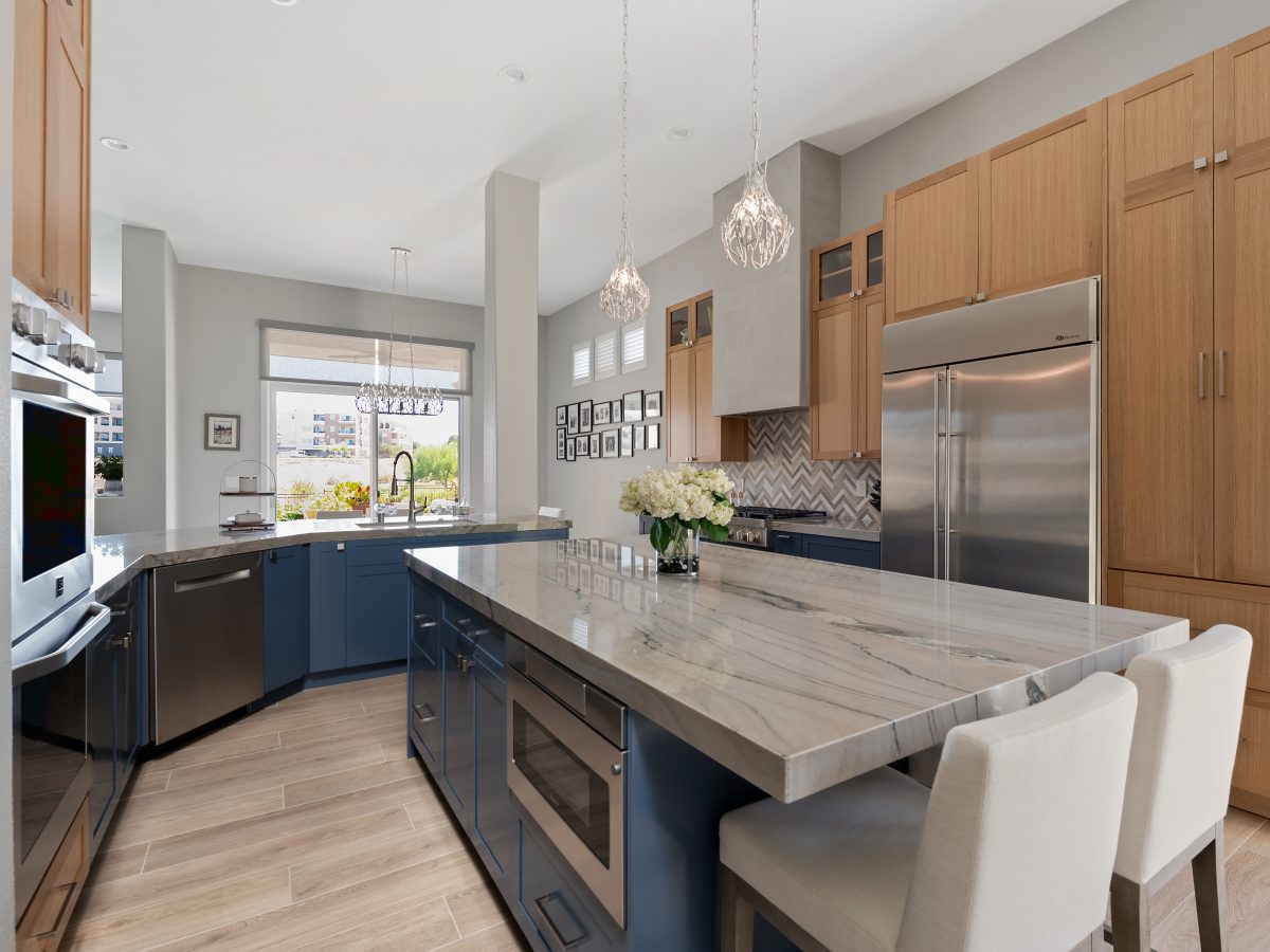 Kitchen with quartzite island, dark blue and warm oak cabinetry, stone herringbone backsplash — Reveal Interior Design Las Vegas