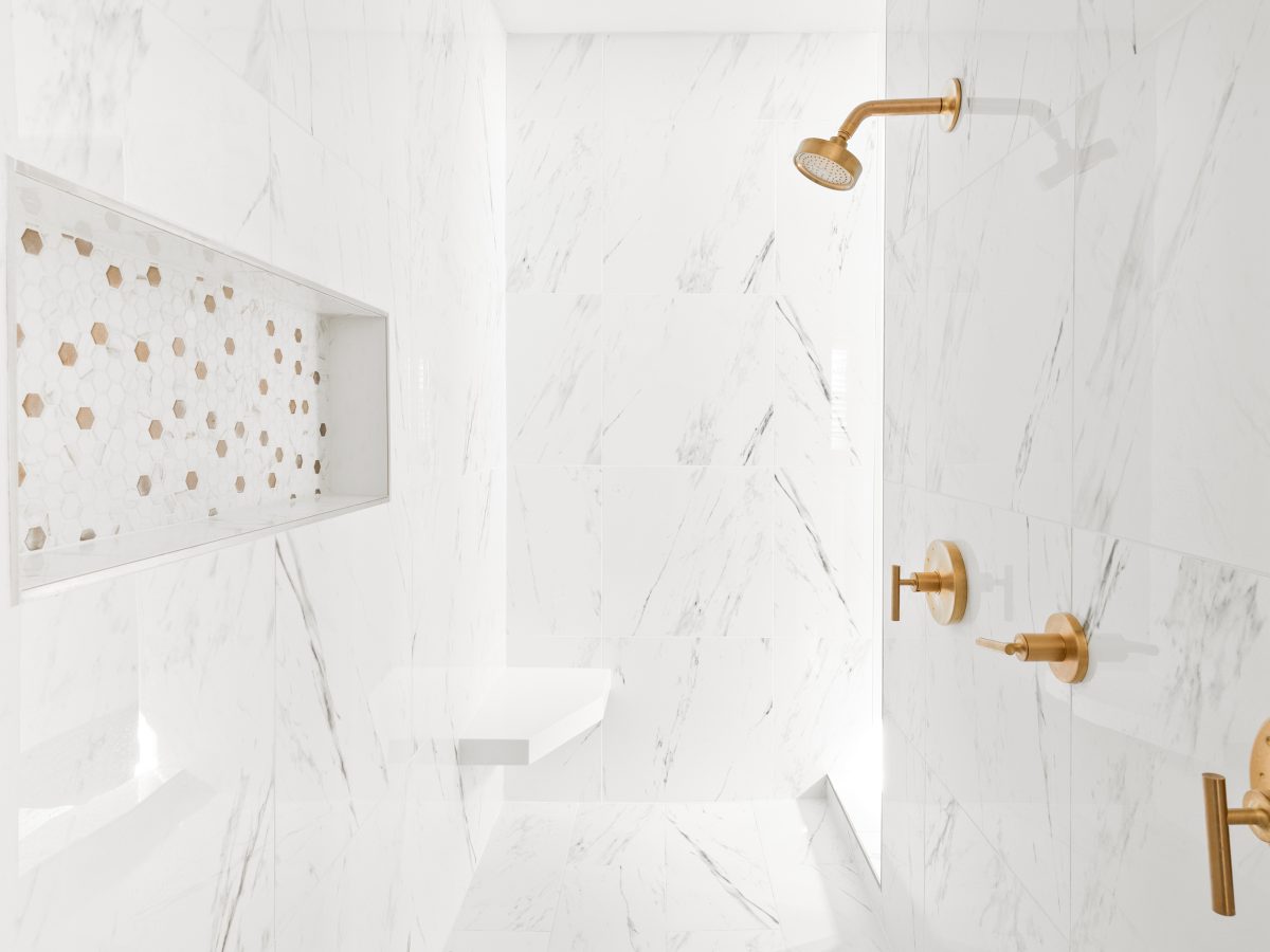 Primary bathroom shower with Calacatta-look porcelain tile walls and brushed gold fixtures — Reveal Interior Design Las Vegas