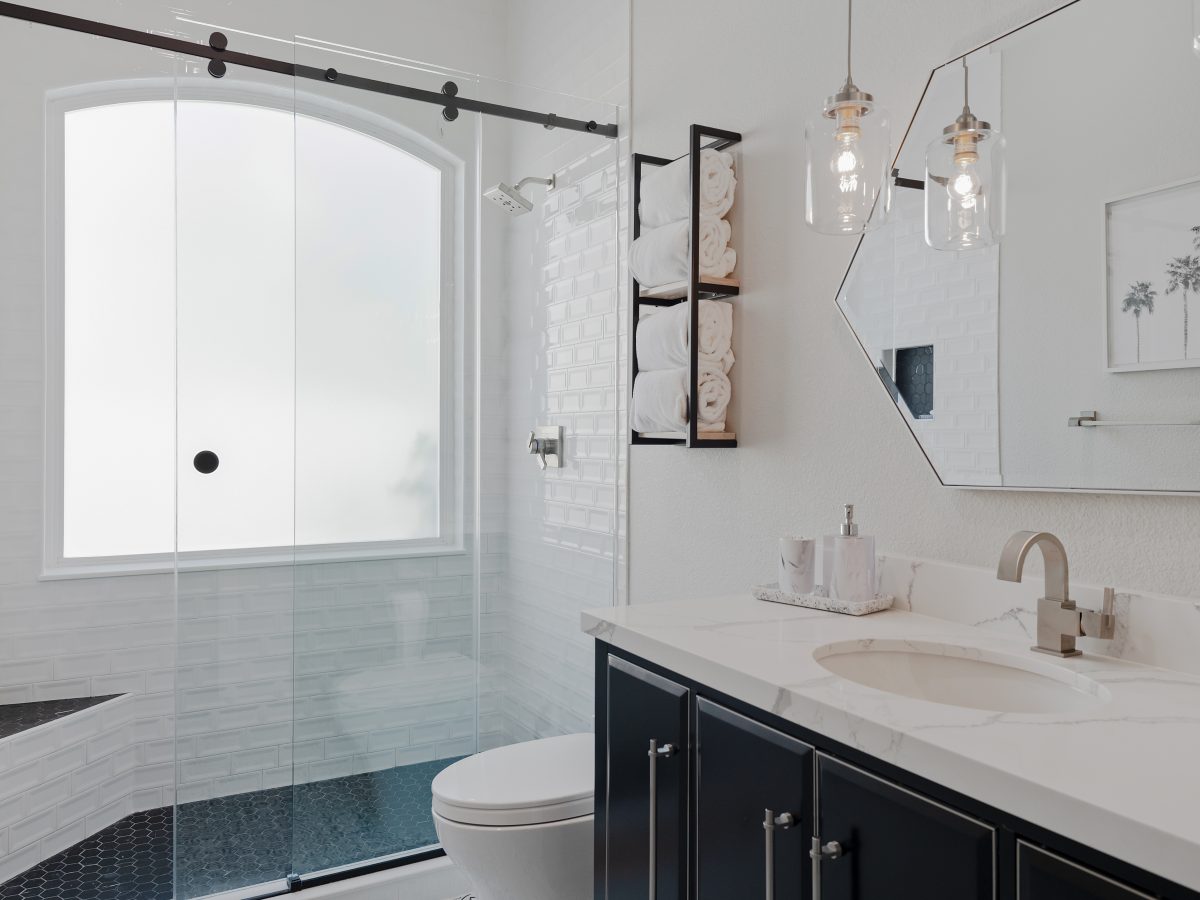 Hall bathroom with furniture-style vanity, quartz countertop, and glass-enclosed subway tile shower — Reveal Interior Design Las Vegas