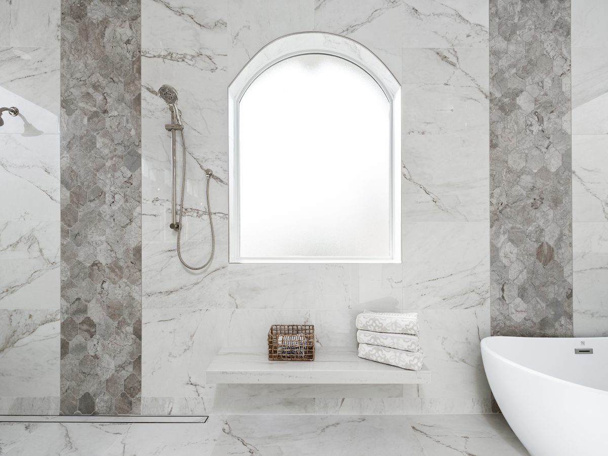 Transitional wet room primary bathroom with marble-look porcelain tile and Taj Mahal quartzite bench — Reveal Interior Design Las Vegas