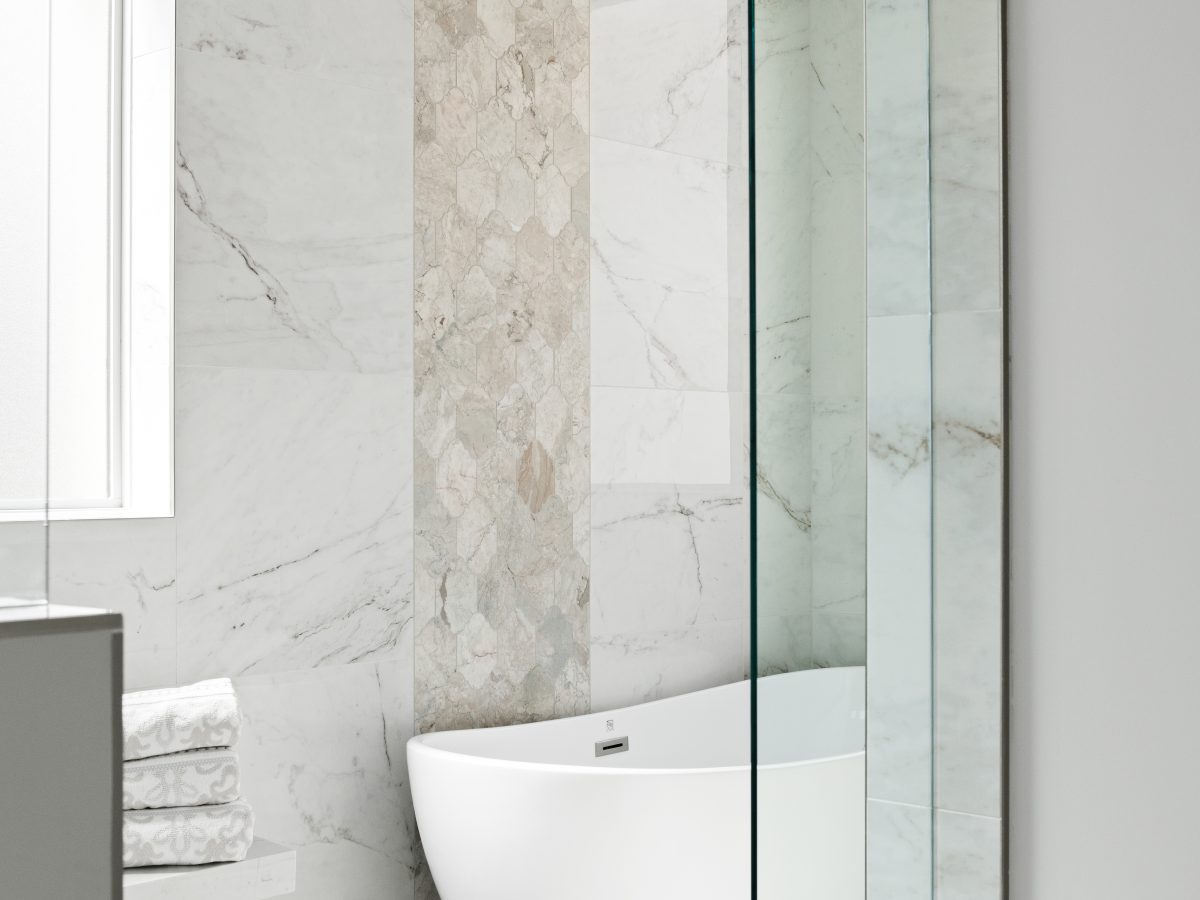 Transitional primary bathroom wet room with freestanding tub, marble-look porcelain tile, and vertical accent band — Reveal Interior Design Las Vegas
