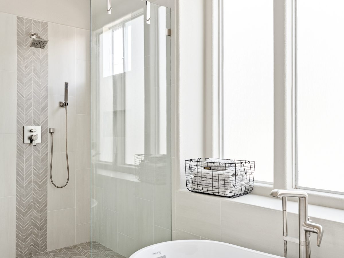 Primary bathroom with freestanding soaking tub, glass walk-in shower, and herringbone porcelain accent tile — Reveal Interior Design Las Vegas