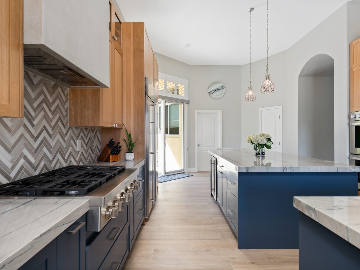Kitchen with blue base cabinets, warm oak uppers, and quartzite countertops — Reveal Interior Design Las Vegas