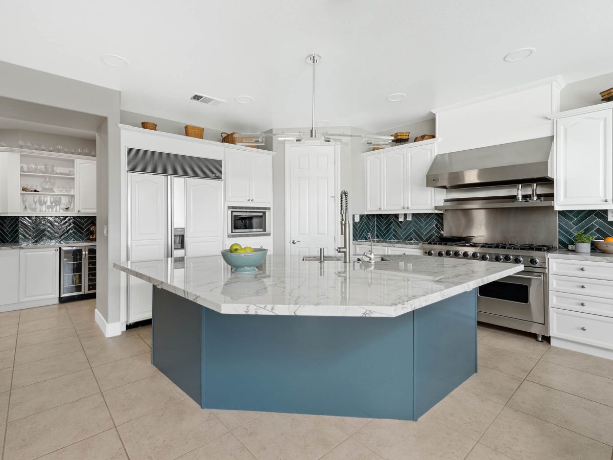Luxury kitchen with teal painted island, blue-veined quartzite countertops, and herringbone backsplash — Reveal Interior Design Las Vegas