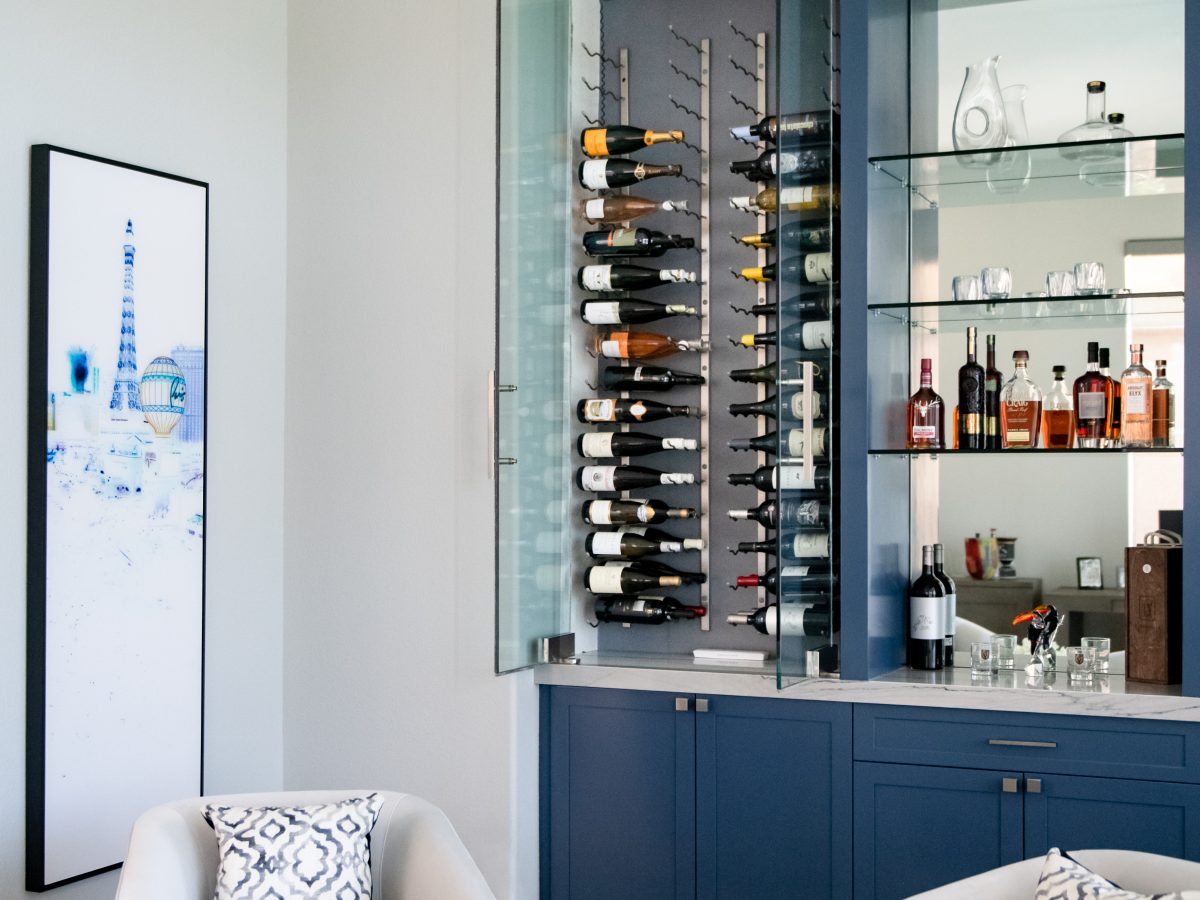 Lounge bar with blue cabinetry, glass-enclosed dual-zone wine storage and mirrored shelving — Reveal Interior Design Las Vegas
