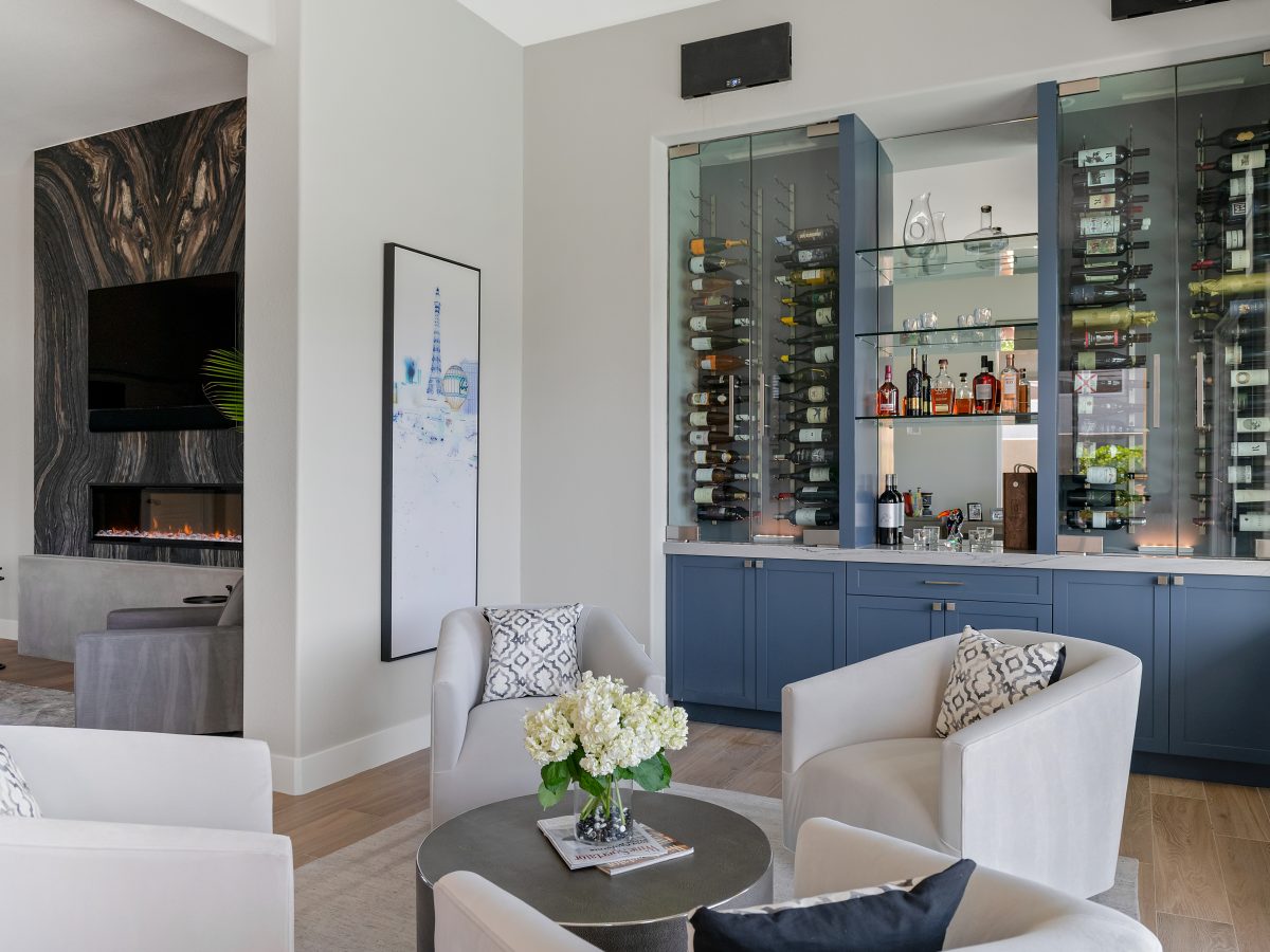Lounge bar with blue cabinetry, glass-enclosed dual-zone wine coolers, and swivel seating — Reveal Interior Design Las Vegas