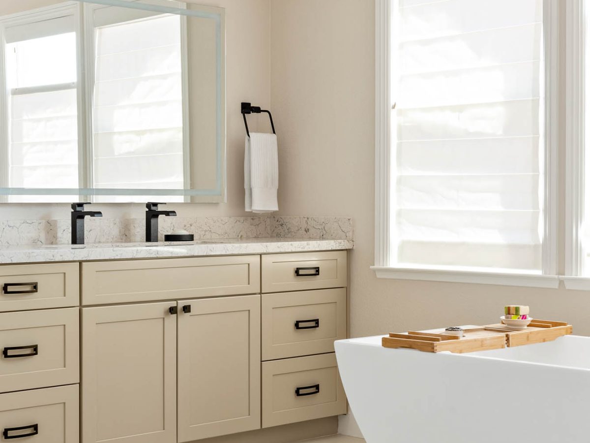 Primary bathroom with warm beige cabinetry, quartz countertops, and freestanding tub — Reveal Interior Design Las Vegas