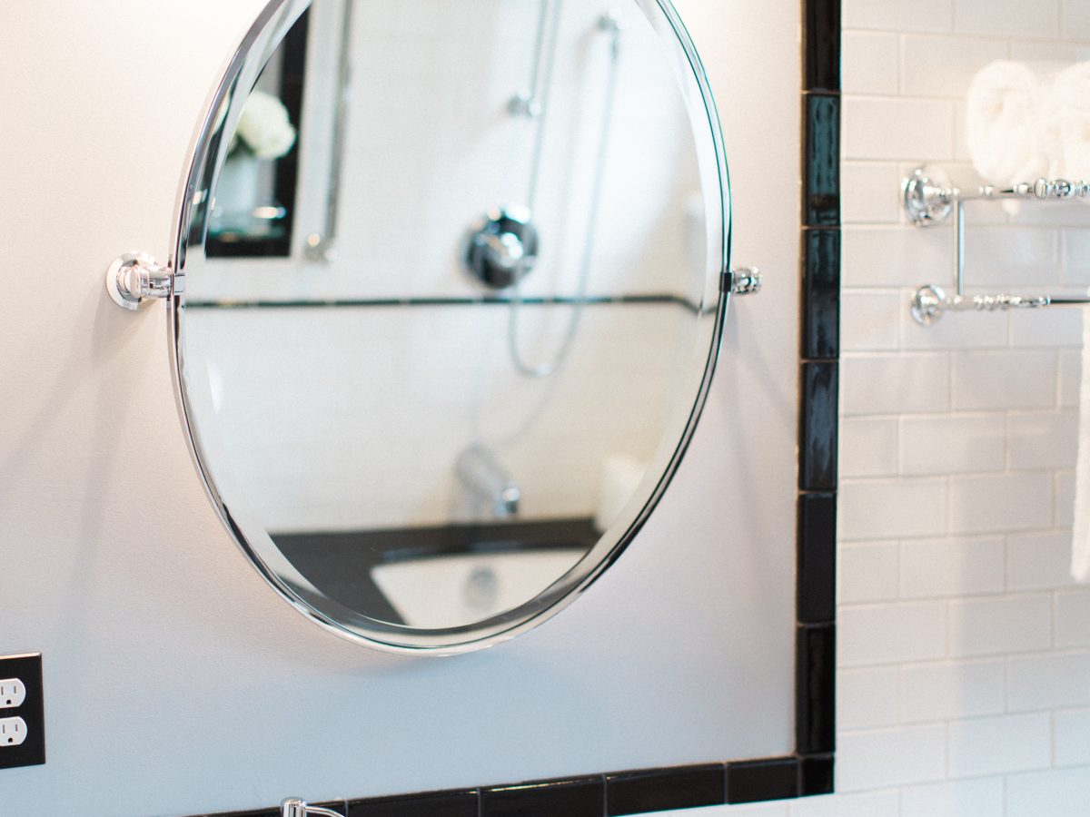 Classic black-and-white bathroom with oval tilt mirror, chrome fixtures, and subway tile wainscoting — Reveal Interior Design Las Vegas
