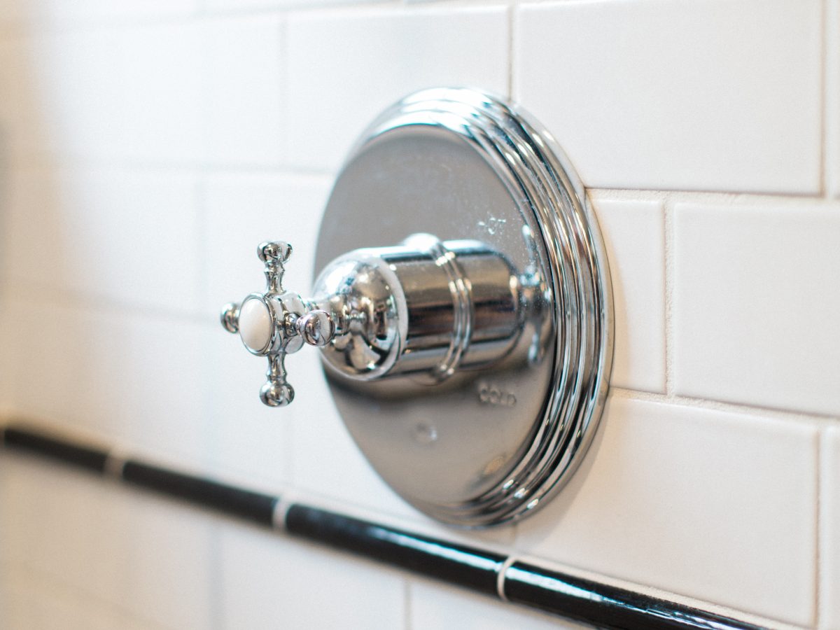 Vintage bathroom shower valve with chrome cross-handle on white subway tile — Reveal Interior Design Las Vegas
