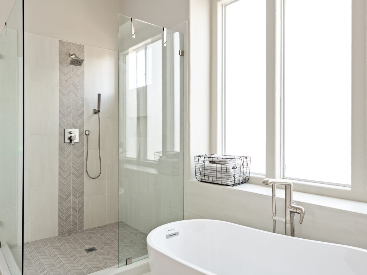 Primary bathroom with freestanding soaking tub, glass-enclosed shower, and porcelain tile — Reveal Interior Design Las Vegas