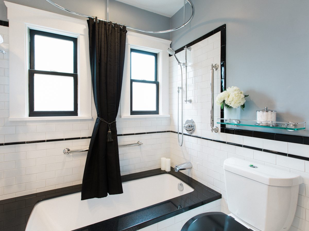 1920s-style black and white bathroom with black granite tub surround and subway tile wainscoting — Reveal Interior Design Las Vegas